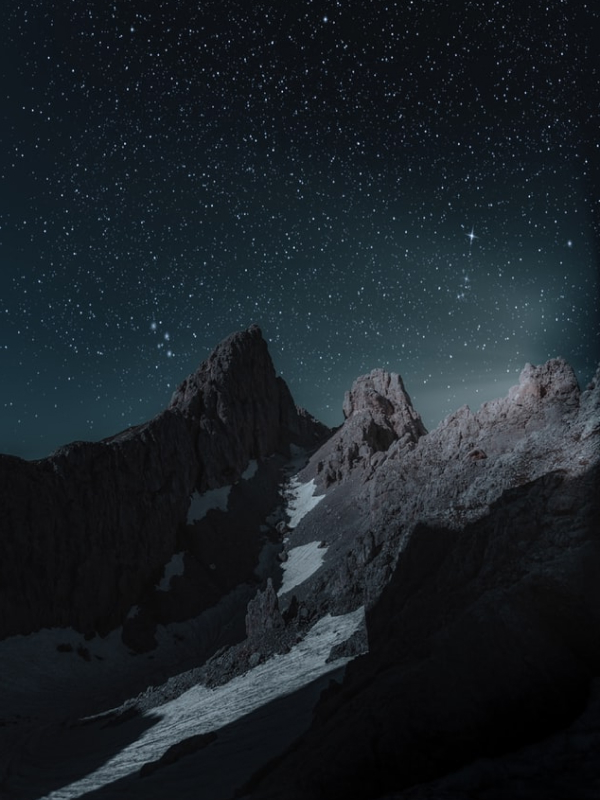 Night falls over the mountains, revealing a starry sky that contrasts with the dark, snowy peaks. The stars seem almost within reach, touching the summits. This image inspires silence, awe, and reflection under the vast universe. A stunning nighttime portrait of majestic isolation and cosmic beauty.